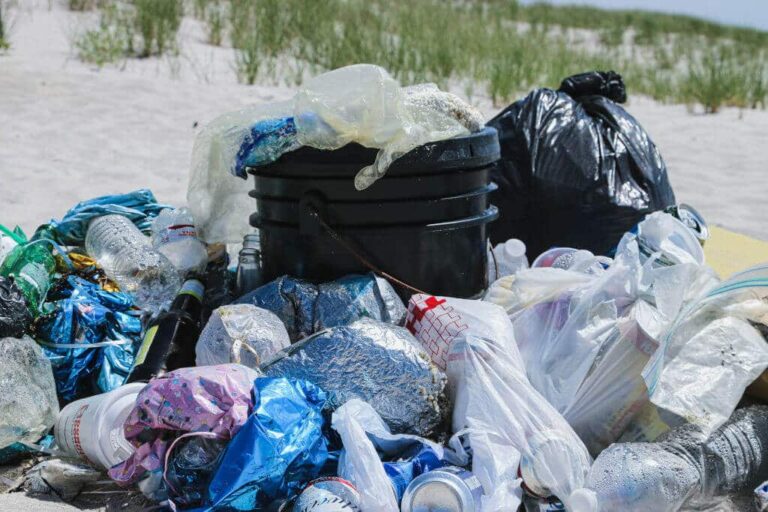 Plastic shopping bags | The Interfaith Center for Sustainable Development Pile of trash and plastic bags on a sandy beach, including bottles and a black bucket, likely litter from a cleanup effort.